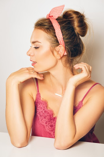 Žena s rozcuchaným drdolom a ružovou šatkou vo vlasoch.