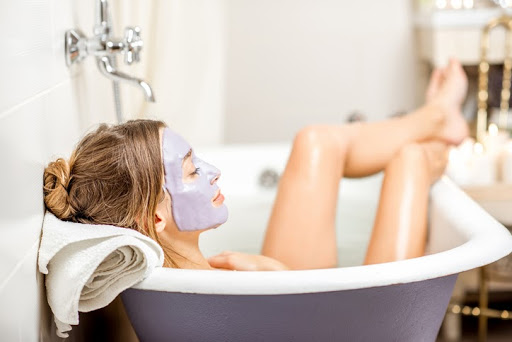 Žena ležiaca vo vani s pleťovou maskou na tvári a s vyloženými nohami.